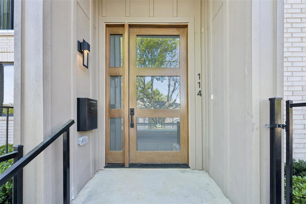 Entry featuring a wood-finish door with three glass panels, a matching glass sidelight, vertical board-and-batten siding, matte black wall-mounted lantern lighting, and a modern black metal mailbox