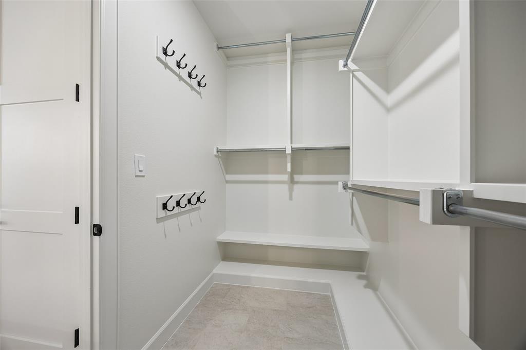 Walk-in closet featuring white built-in shelving, dual-tier metal hanging rods, tiered fixed wall hooks, and light-toned tile flooring