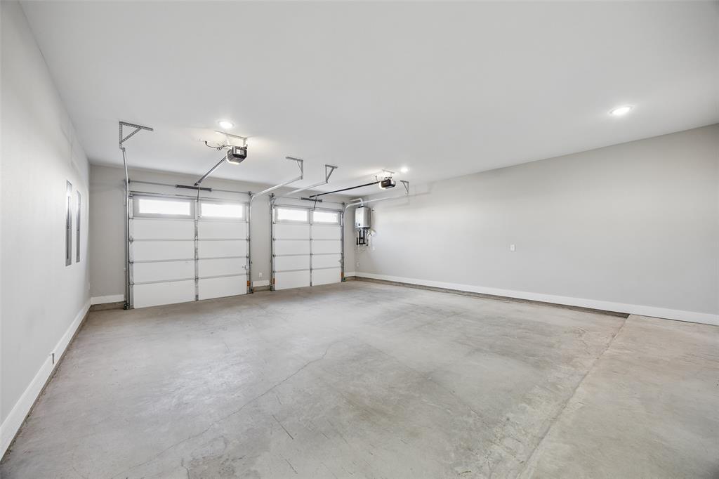 Multi-car garage featuring recessed lighting, two white paneled overhead doors with transom windows, and a wall-mounted tankless water heater