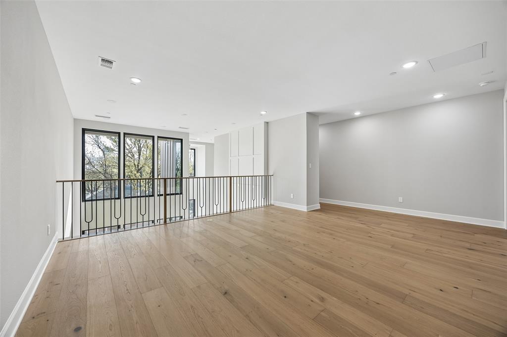Open-concept interior featuring light wood-finish flooring, recessed lighting, decorative wall paneling, and a metal railing