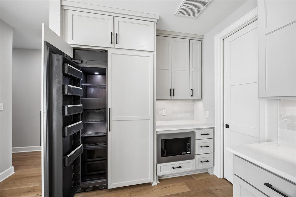 Custom cabinetry featuring a paneled refrigerator, built-in microwave, light-toned stone countertops, and matte black hardware