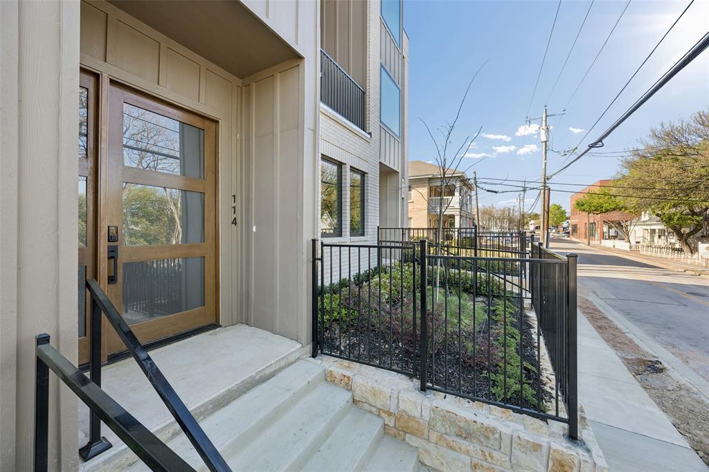 Modern entrance featuring a wood-panel door with glass inserts, concrete steps with black metal handrails, a stone-veneer retaining wall, and black metal fencing
