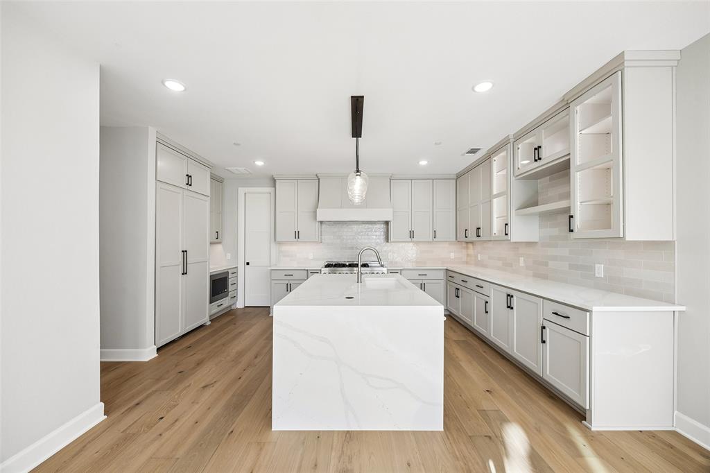 Kitchen featuring a central island with a quartz countertop, custom cabinetry, wood-finish flooring, recessed lighting, and a ceramic tile backsplash