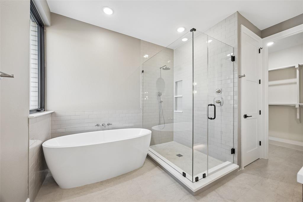 Freestanding soaking tub, glass-enclosed walk-in shower with subway tile surround, recessed wall niche, and matte black hardware