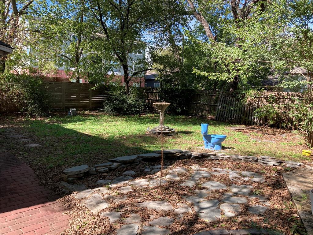 Private backyard featuring a stone-edged patio, brick masonry path, stone birdbath, and perimeter wood fencing