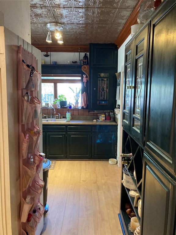 Kitchen featuring a coffered tin ceiling, dark cabinetry with glass-panel detailing, built-in wine storage, wood-finish flooring, and a flush-mount track light fixture