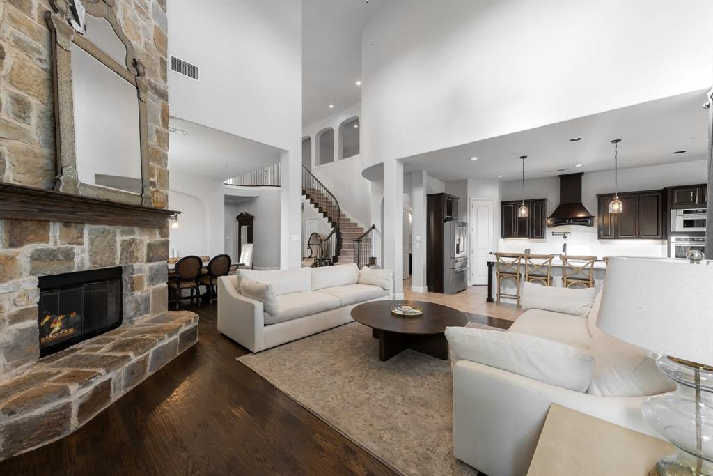 Floor-to-ceiling stone fireplace, dark wood-finish flooring, soaring ceilings, curved staircase with iron railing, and gourmet kitchen with dark cabinetry and breakfast bar