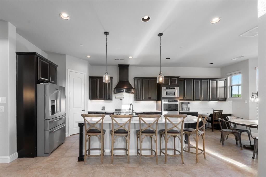 Kitchen featuring dark wood cabinetry, a central stone-topped island with seating, stainless steel appliances, a built-in oven, and recessed lighting