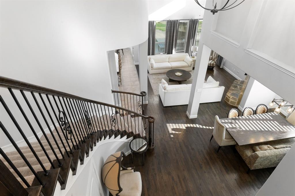 Grand staircase featuring dark wood treads and decorative wrought iron balustrades, set within an open-concept interior with vaulted ceilings, wood-finish flooring, and a stone-accented hearth