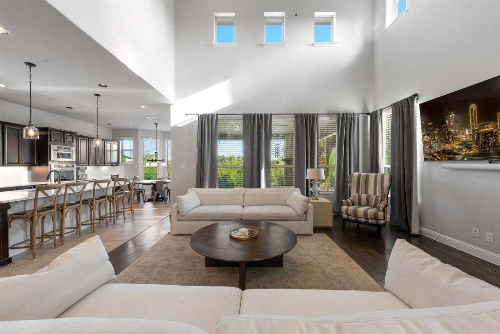 Double-height ceilings, expansive window wall with transoms, dark-toned cabinetry, kitchen island with seating, and wood-finish flooring