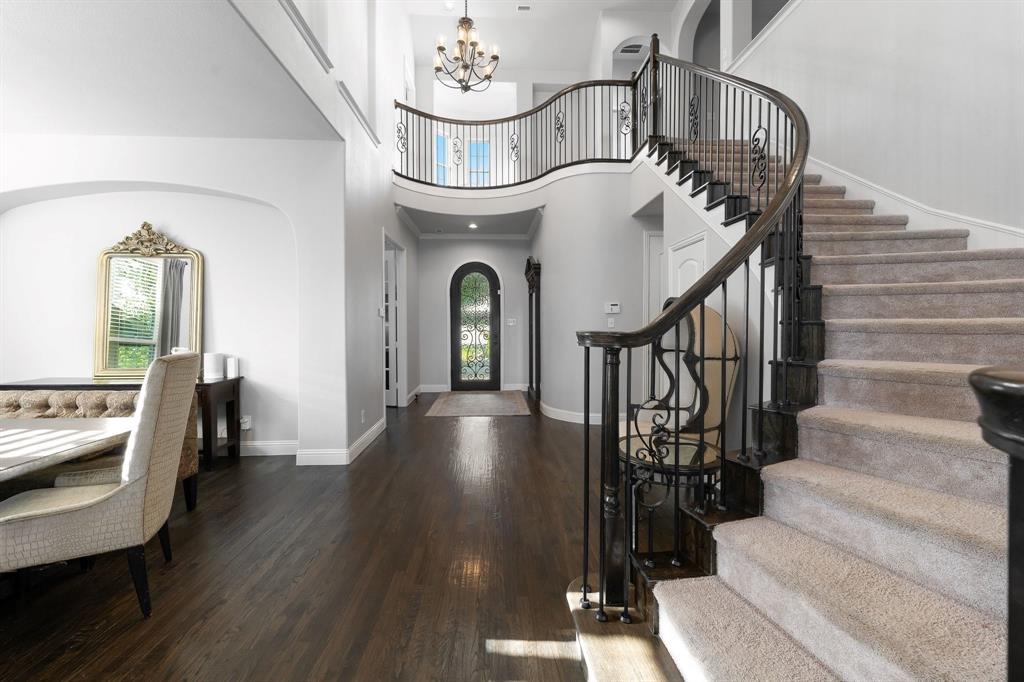 Grand foyer featuring a curved staircase with iron balusters, dark wood-finish flooring, an arched entryway with a glass-paneled door, and a multi-tiered chandelier