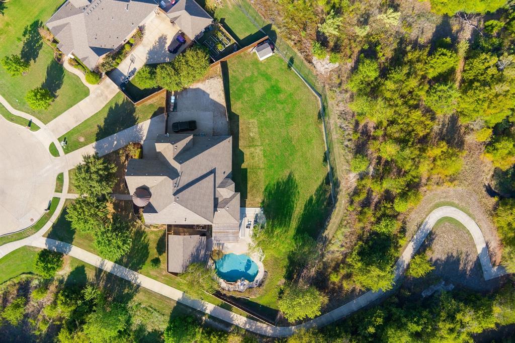 Aerial perspective of a property featuring an in-ground pool, expansive grass lawn, paved driveway, and perimeter wood fencing