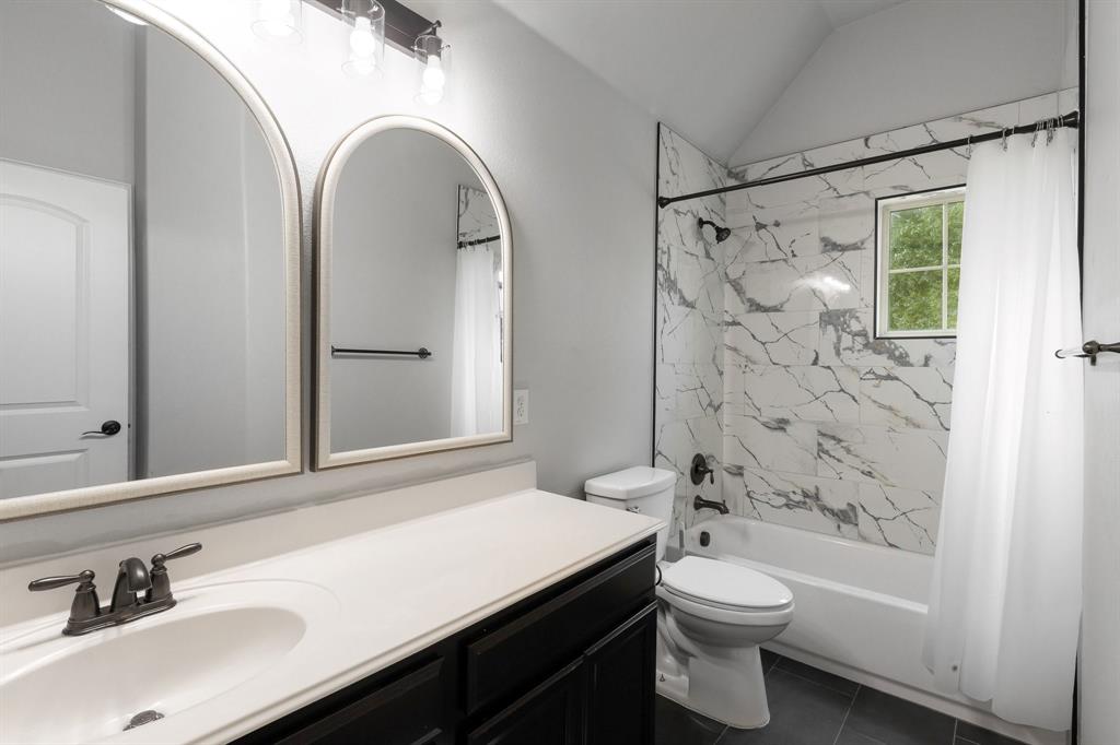 Completely renovated bathroom!  Dark-toned cabinetry with a white countertop, dual arched wall mirrors, and a tub-shower combination featuring large-format stone-patterned tile surrounds