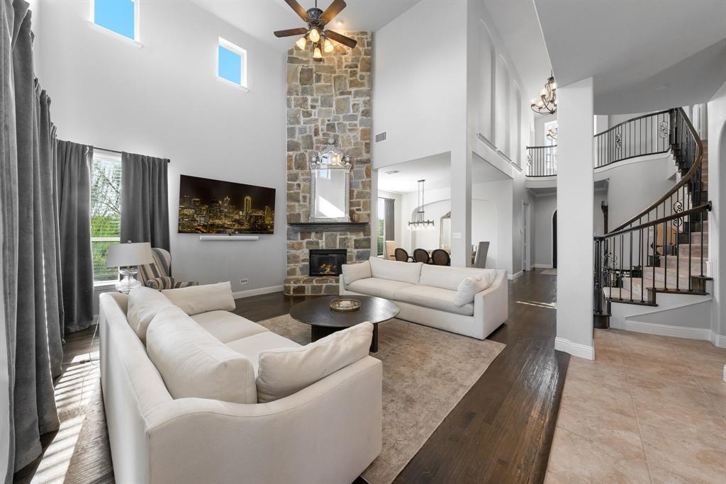 Two-story living area featuring a floor-to-ceiling stone fireplace, wood-finish flooring, double-height ceilings, and a curved staircase with iron balusters