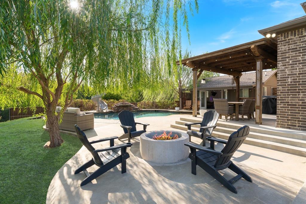 Oversized Backyard featuring a concrete patio with a circular fire pit, an in-ground swimming pool with a stone water feature, a covered pergola, and a brick exterior