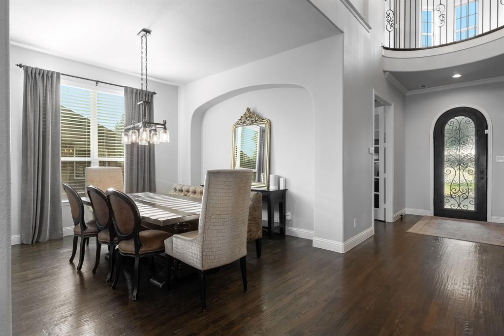 Dining area featuring arched wall detailing, wood-finish flooring, and a multi-light pendant fixture, complemented by an entry featuring an arched door with iron decorative insets and a curved balcony overlook