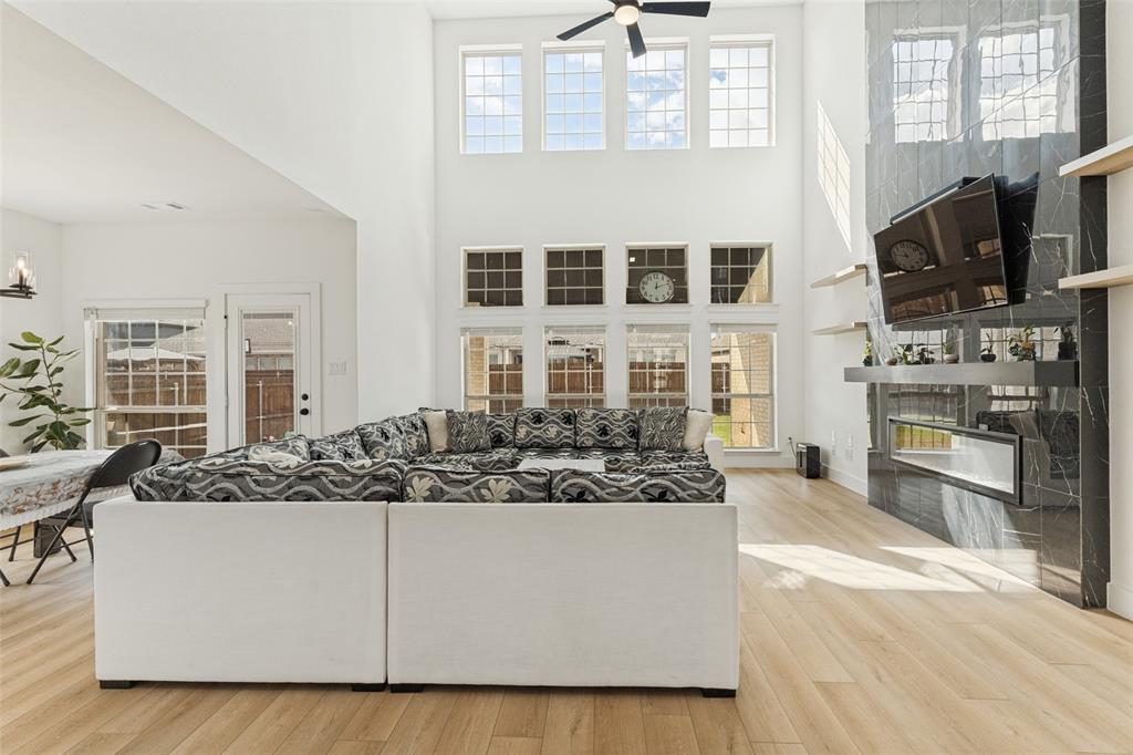 Double-height ceilings, floor-to-ceiling stone-finish fireplace, built-in horizontal shelving, wood-finish flooring, and expansive grid windows