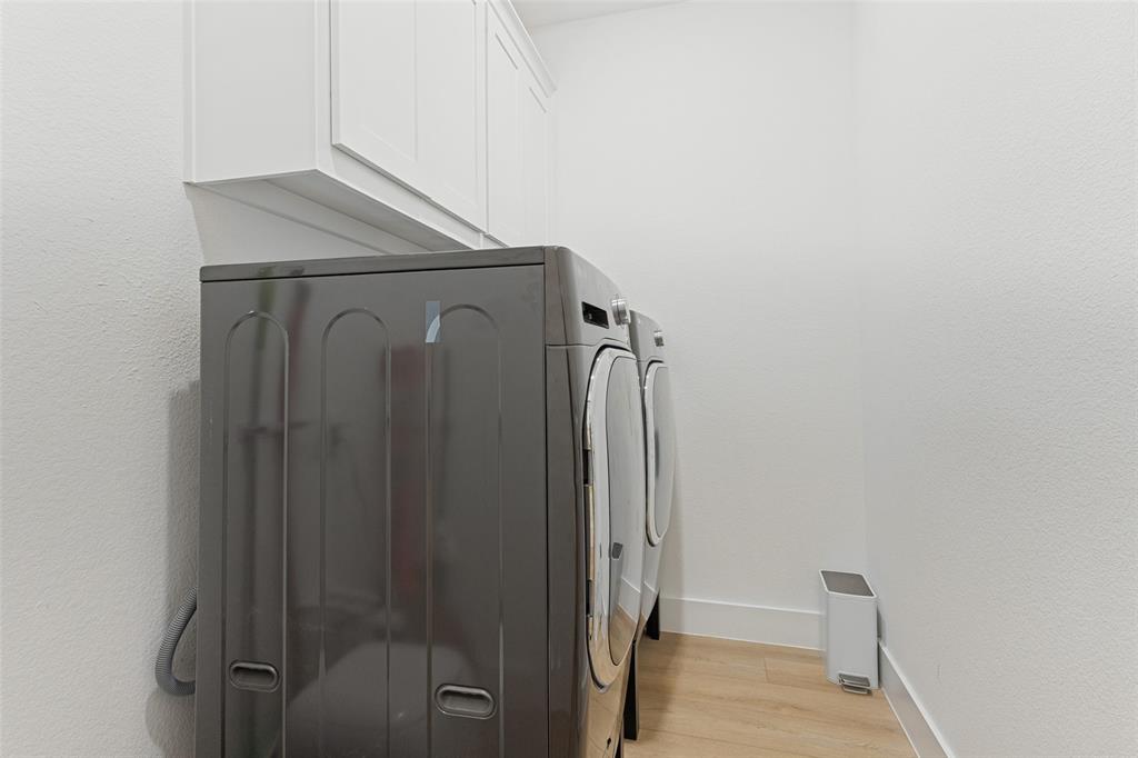 Laundry room featuring white wall-mounted cabinetry and wood-finish flooring
