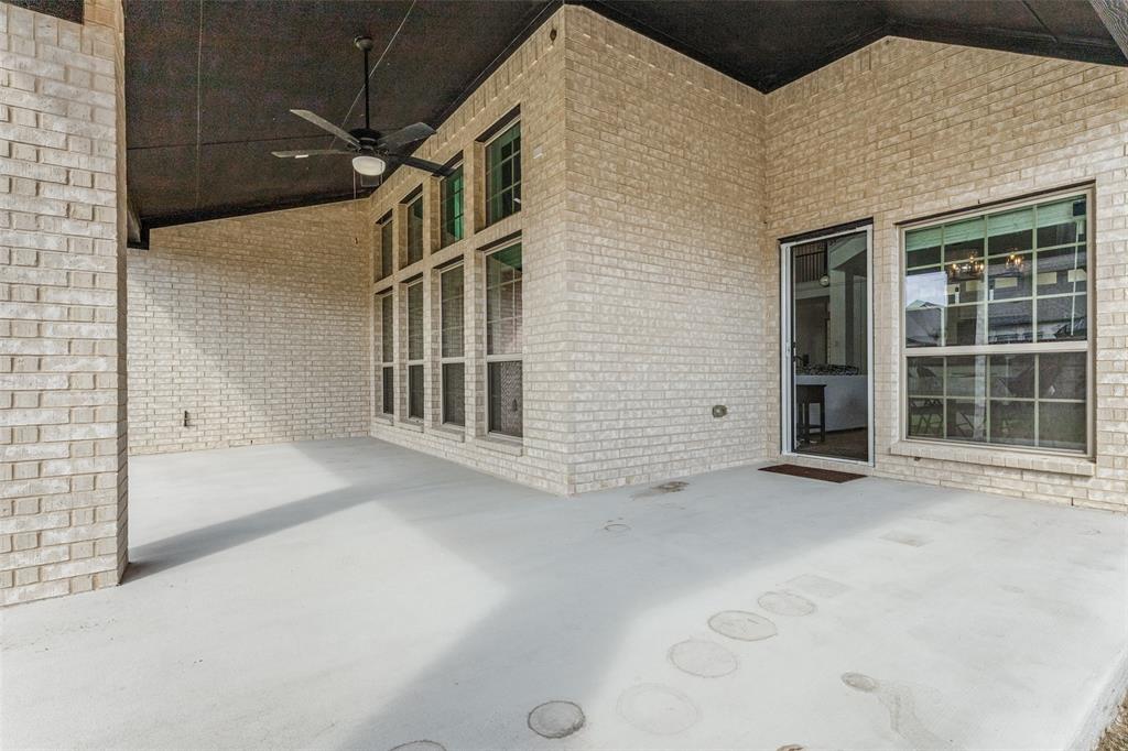 Covered patio featuring light-colored brick exterior walls, a dark-toned ceiling, a ceiling fan, and large grid-pattern windows