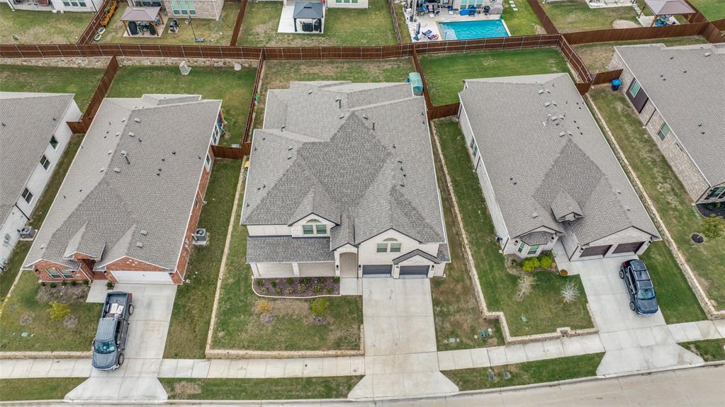 Aerial perspective of a multi-gabled residence featuring a multi-car garage, concrete driveway, and a fenced rear lawn