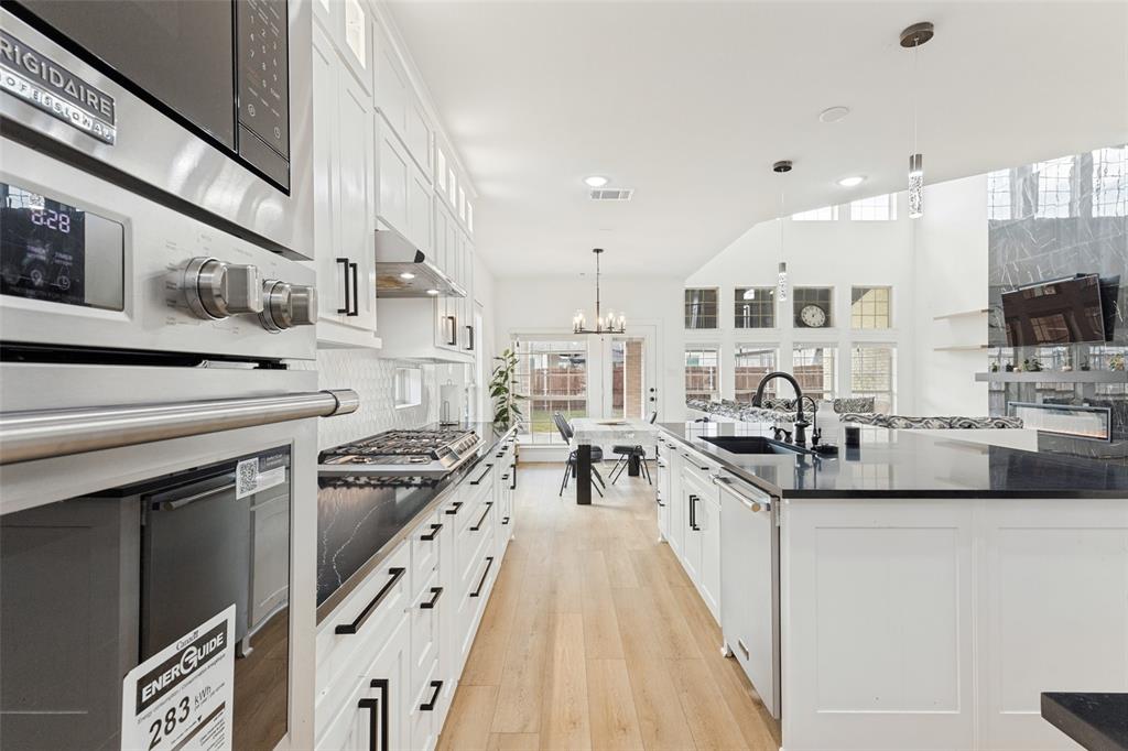 Kitchen featuring white shaker-style cabinetry, dark stone countertops, stainless steel appliances, wood-finish flooring, and a large center island with an undermount sink