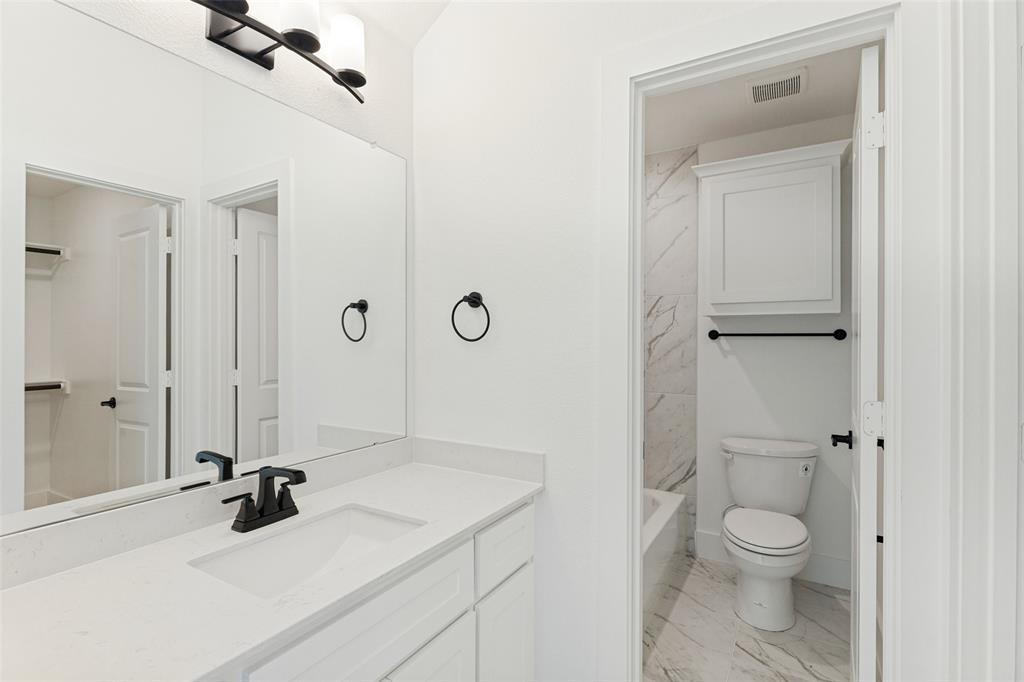 Bathroom featuring a vanity with a stone countertop, an integrated rectangular sink, matte black plumbing fixtures, an expansive wall-to-wall mirror, and overhead lighting