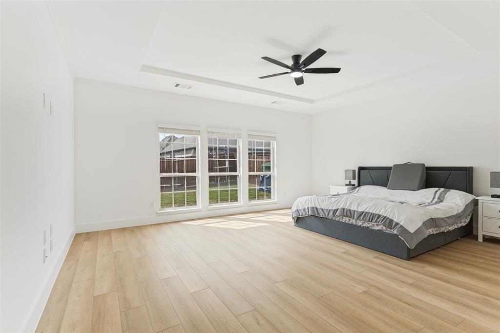 Spacious interior featuring wood-finish flooring, a tray ceiling, three large windows, and a matte black ceiling fan