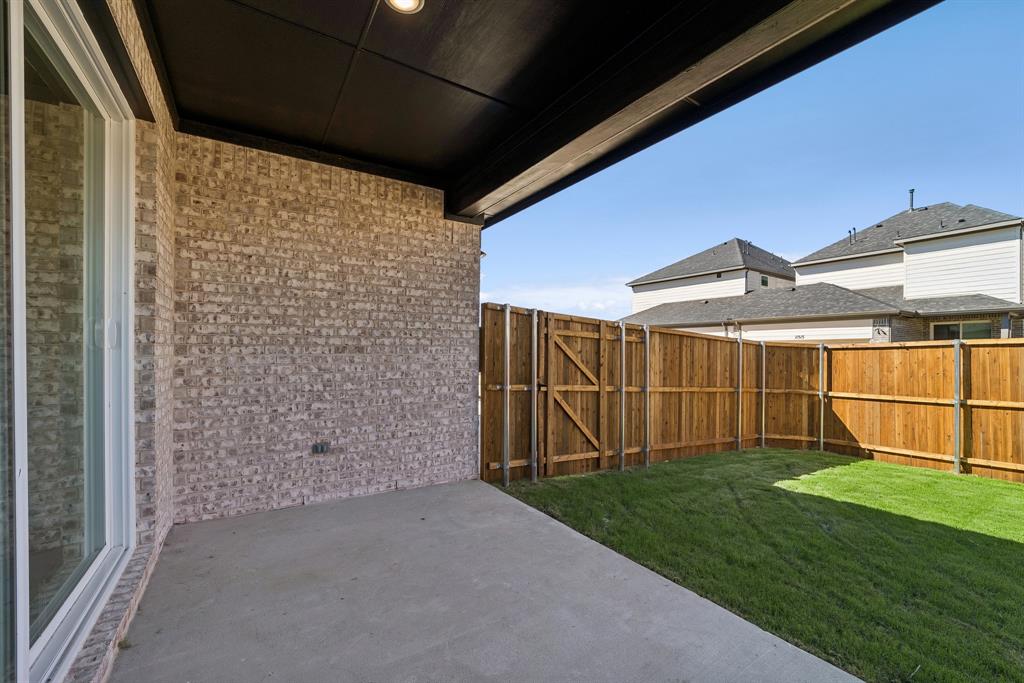 Covered patio with a concrete surface, light brick exterior wall, and wood privacy fencing enclosing a grass lawn