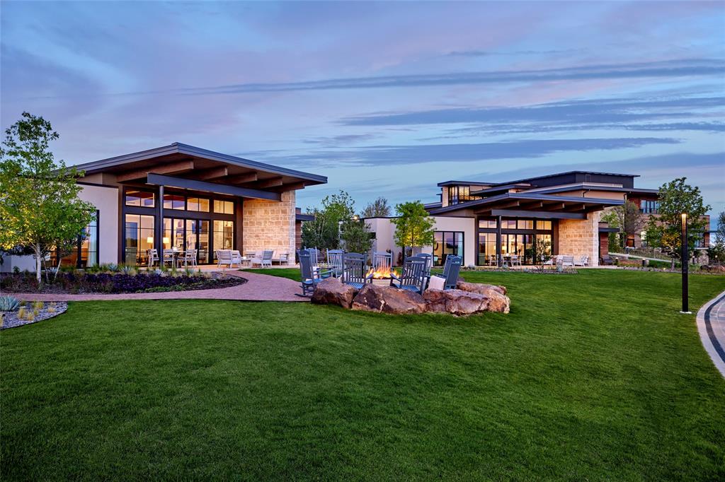 Modern architectural exterior featuring expansive glass walls, horizontal rooflines, stone facade accents, and a stone-encased fire pit set within a landscaped lawn