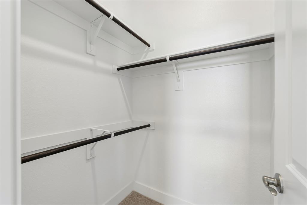 Storage area featuring tiered white shelving and dark-finish clothing rods