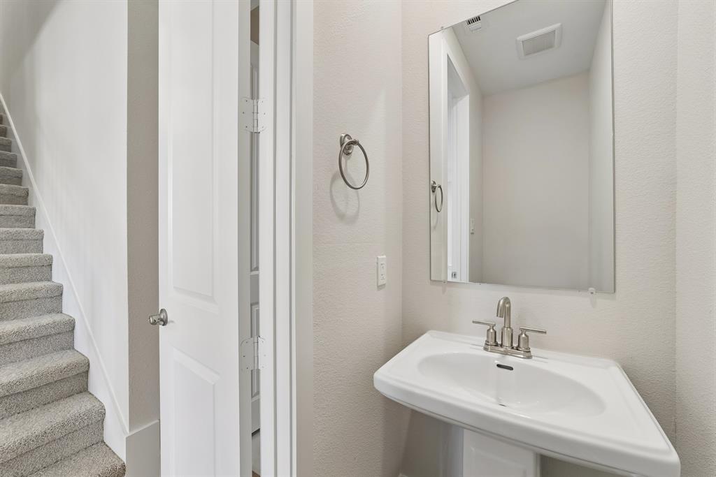 Wall-mounted vanity featuring a pedestal basin, dual-handle metal faucet, rectangular mirror, and circular towel ring