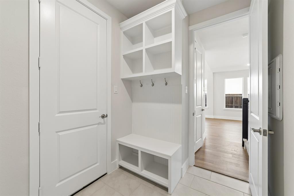 Built-in white storage hall tree featuring upper shelving, metal coat hooks, and a lower bench with cubby storage, complemented by large-format tile flooring and interior panel doors