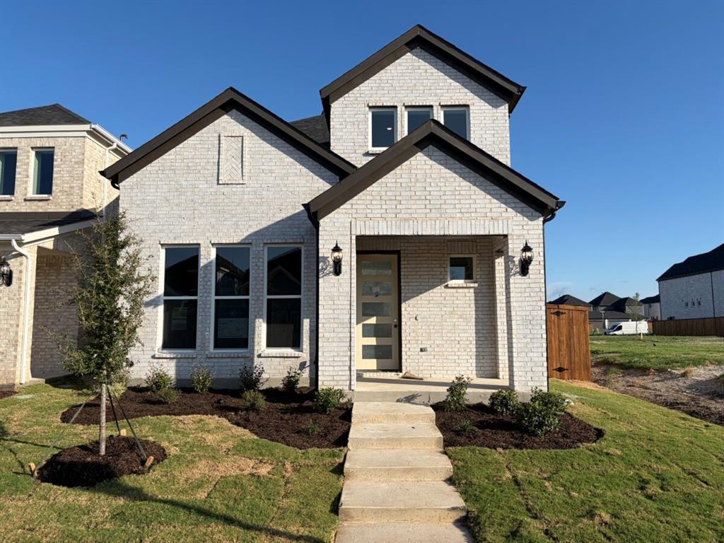 Two-story brick exterior featuring a covered front porch, multi-pane entry door, steep roof pitch, and crisp landscaping