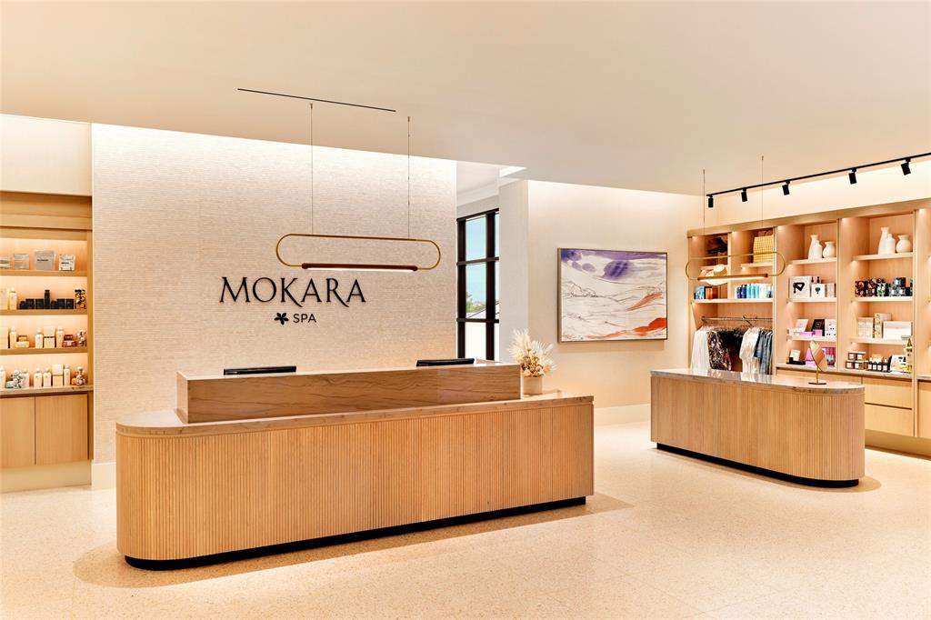 FRISCO PGA Reception area featuring custom wood-veneer cabinetry, integrated stone-surfaced countertops, textured wall detailing, polished light-toned flooring, and minimalist linear pendant lighting