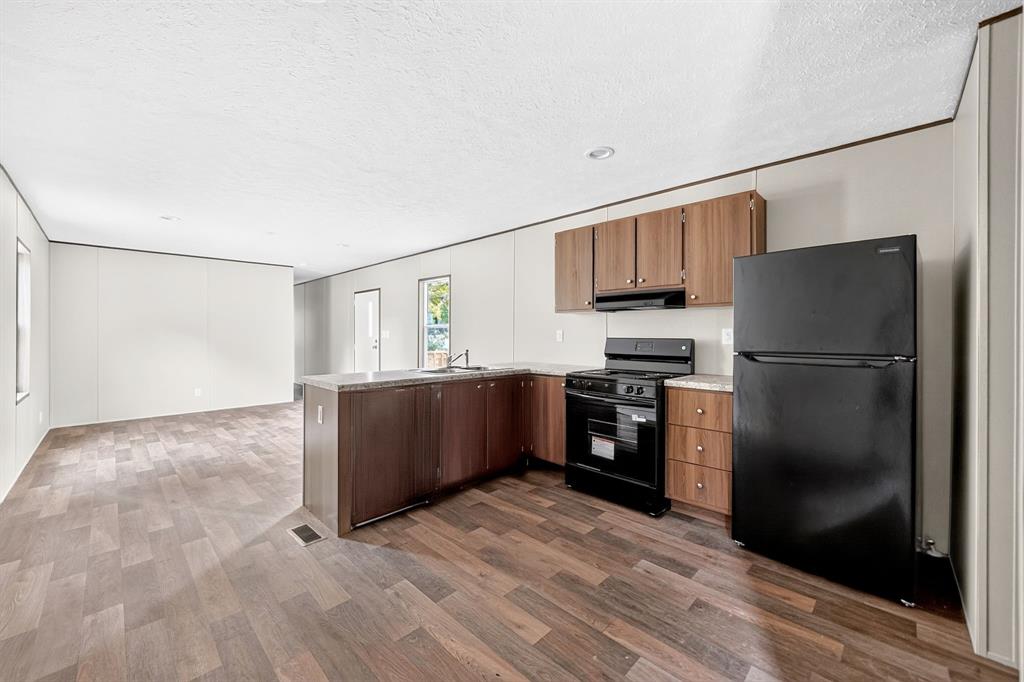 Kitchen featuring wood-finish cabinetry, stone-pattern countertops, and integrated black appliances including a range and refrigerator, complemented by wood-finish flooring