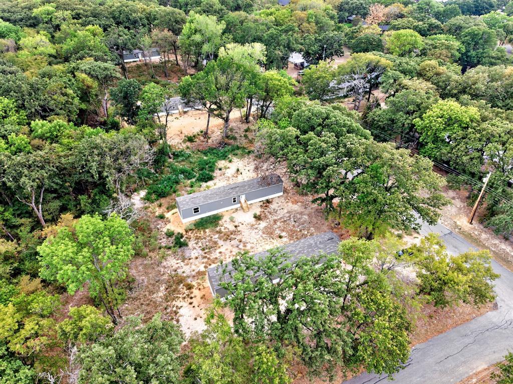 Aerial perspective of a detached residential structure situated on a wooded lot featuring extensive mature tree canopy and paved street access