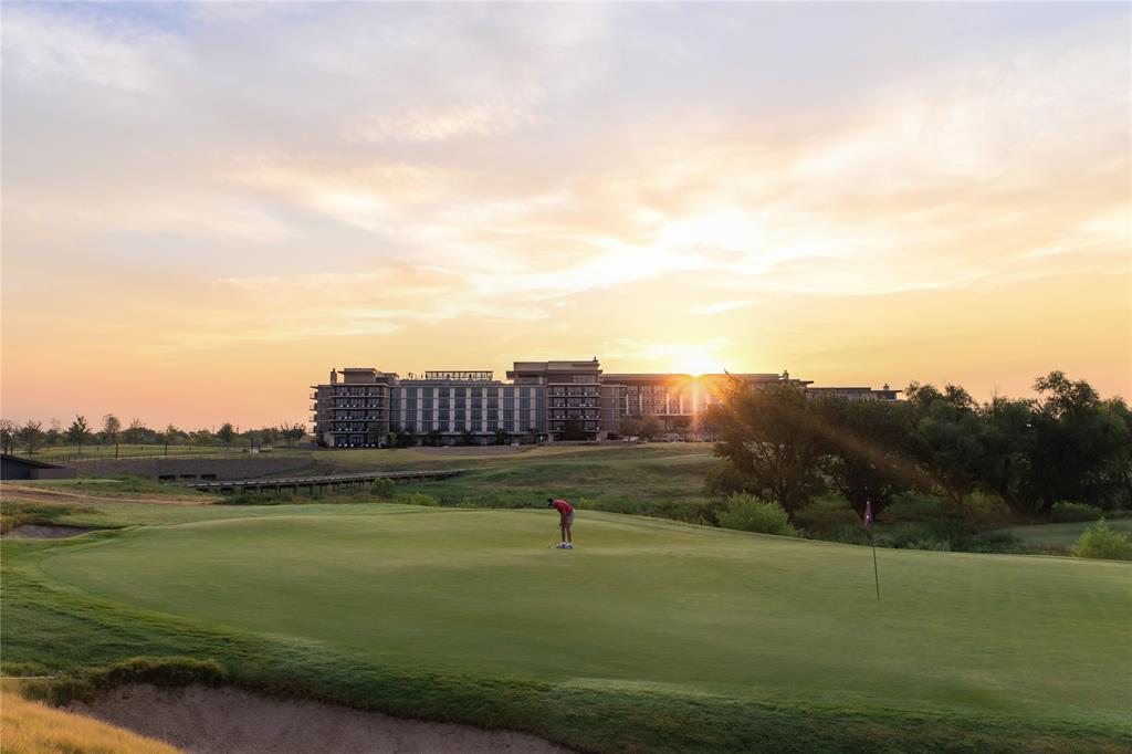 FRISCO PGAGolf course featuring a putting green, sand bunker, and flagstick, set against a backdrop of mature trees and a multi-story building