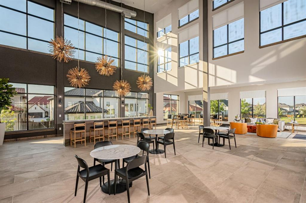 LEXINGTON Community Double-height ceilings with floor-to-ceiling windows, oversized starburst-style pendant lighting, stone-tile flooring, and a long built-in bar counter