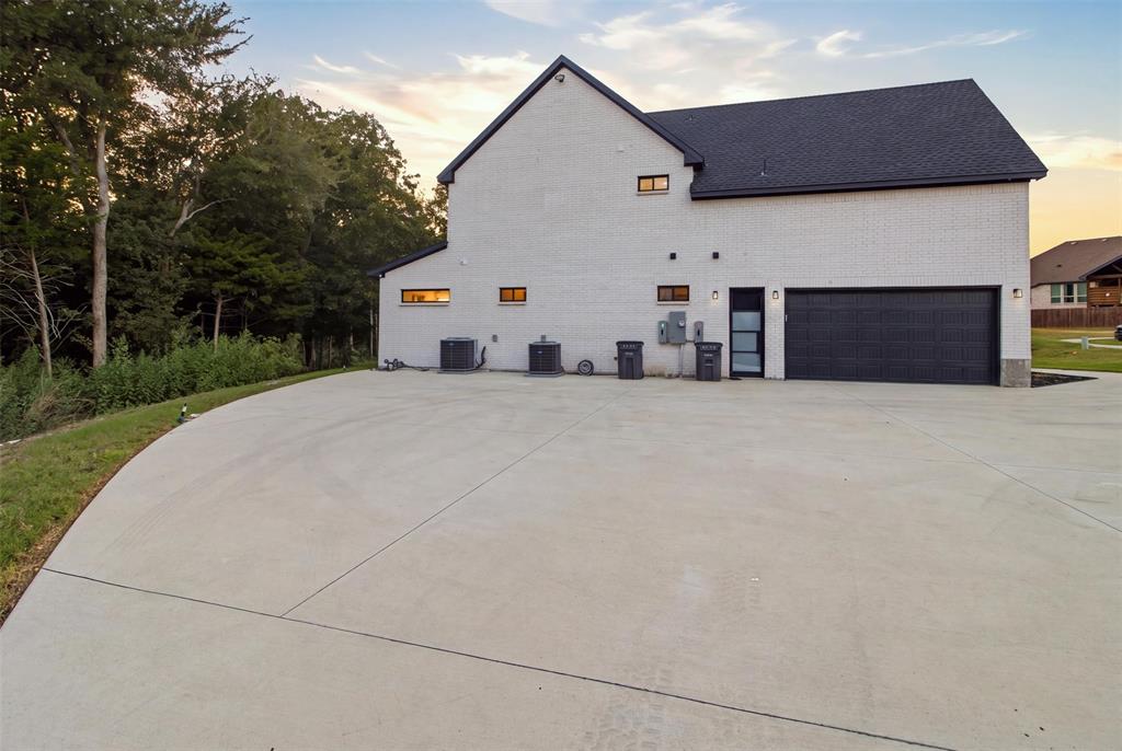 Exterior featuring white painted brick masonry, a gabled roofline, dark-toned garage door, and a spacious concrete driveway