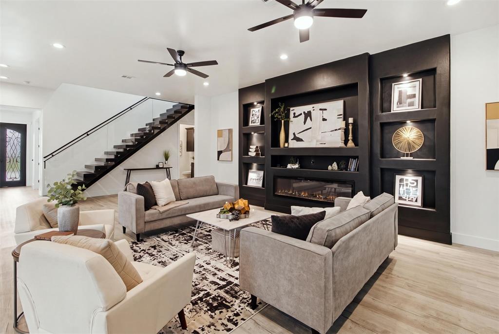 Floor-to-ceiling black feature wall with integrated shelving and fireplace, wood-finish flooring, staircase with glass railing, and ceiling fans
