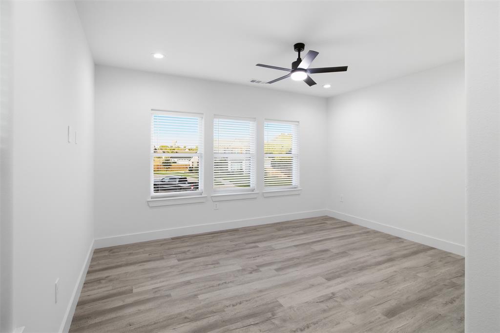 Neutral-toned interior space featuring wood-finish flooring, three double-hung windows with horizontal blinds, recessed lighting, and a matte black ceiling fan with integrated light