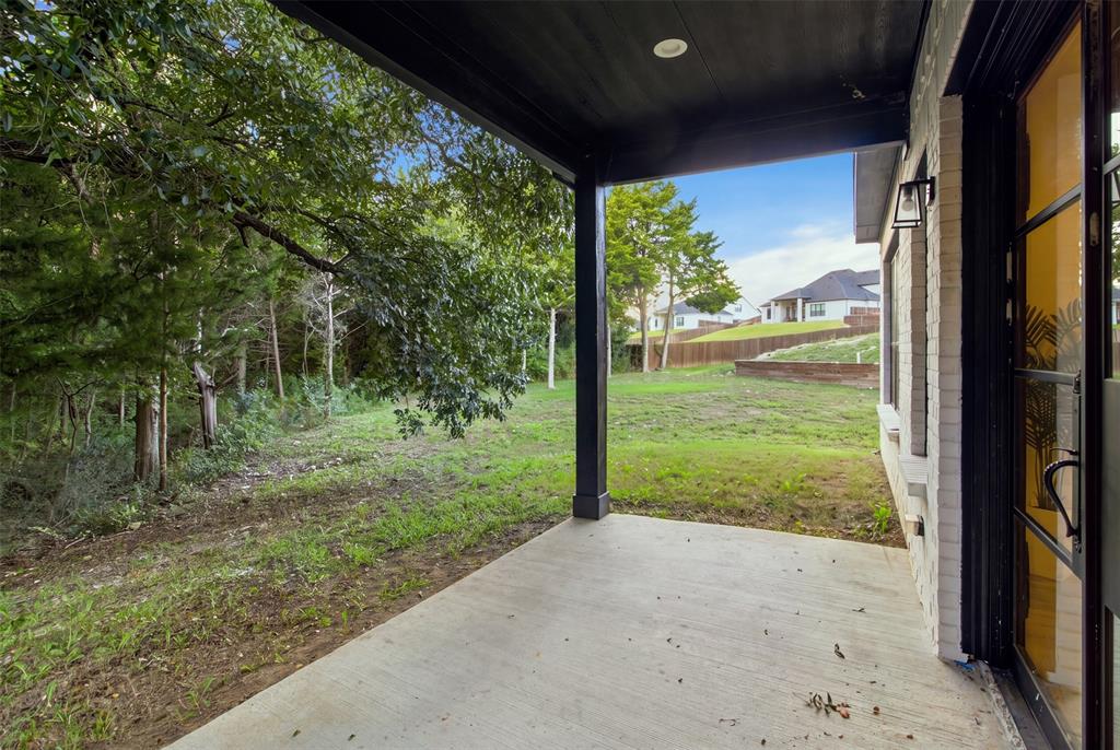 Covered rear patio featuring a concrete floor, black painted support column, recessed lighting, and a brick exterior wall with a metal-framed glass door