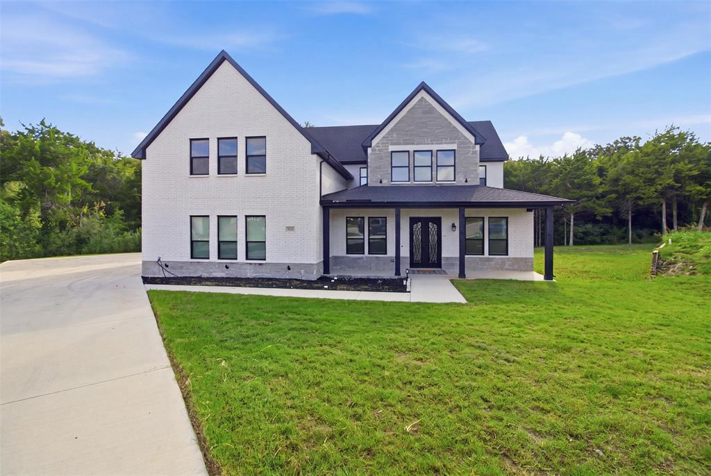 Two-story exterior featuring painted brick facade, dark metal roofing, stone accent detailing, covered front porch, and large multi-pane windows