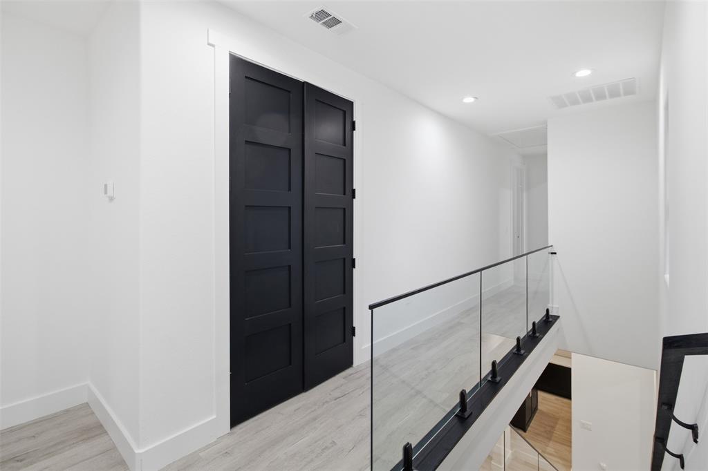 Matte black five-panel double doors, glass panel railing with black hardware, wood-finish flooring, and recessed lighting
