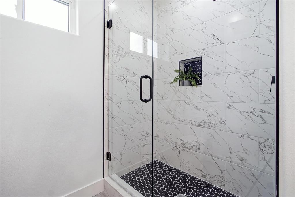Walk-in shower featuring glass door enclosure, large-format veined tile walls, geometric floor tiling, and a built-in recessed niche with dark hexagonal tile detail