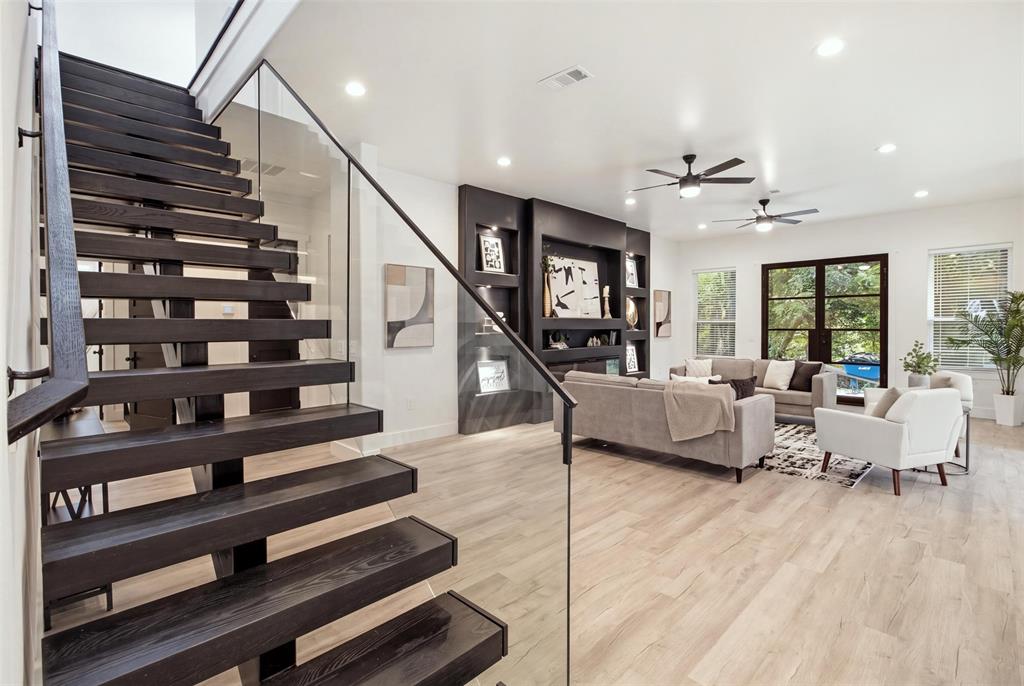 Open-riser staircase with dark wood-finish treads, glass panel railing, recessed wall shelving with integrated lighting, wood-finish flooring, and recessed ceiling lighting