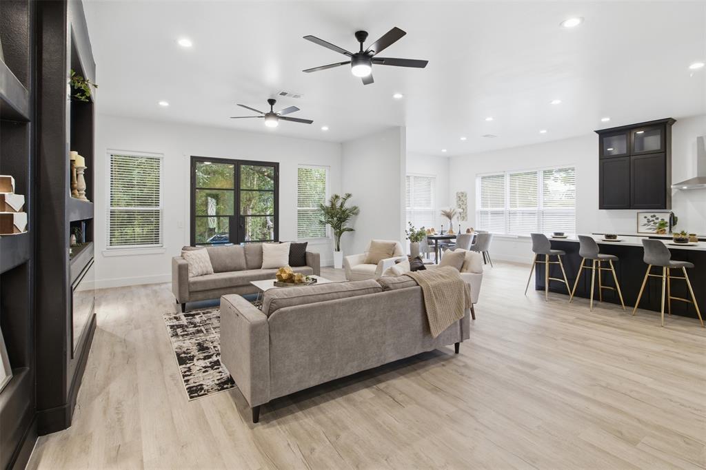 Open-concept interior featuring light wood-finish flooring, recessed lighting, dual ceiling fans, a dark built-in shelving unit, and a kitchen island with dark cabinetry