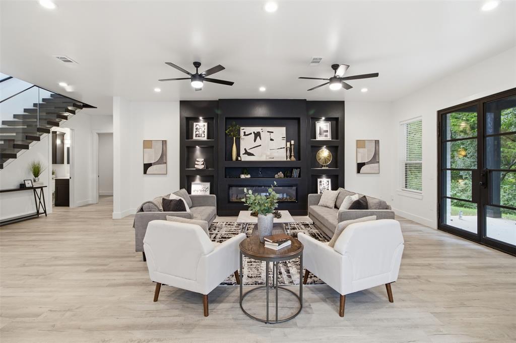 Living area featuring wood-finish flooring, a matte black built-in fireplace with integrated shelving, recessed lighting, double ceiling fans, and black-framed glass paneled doors