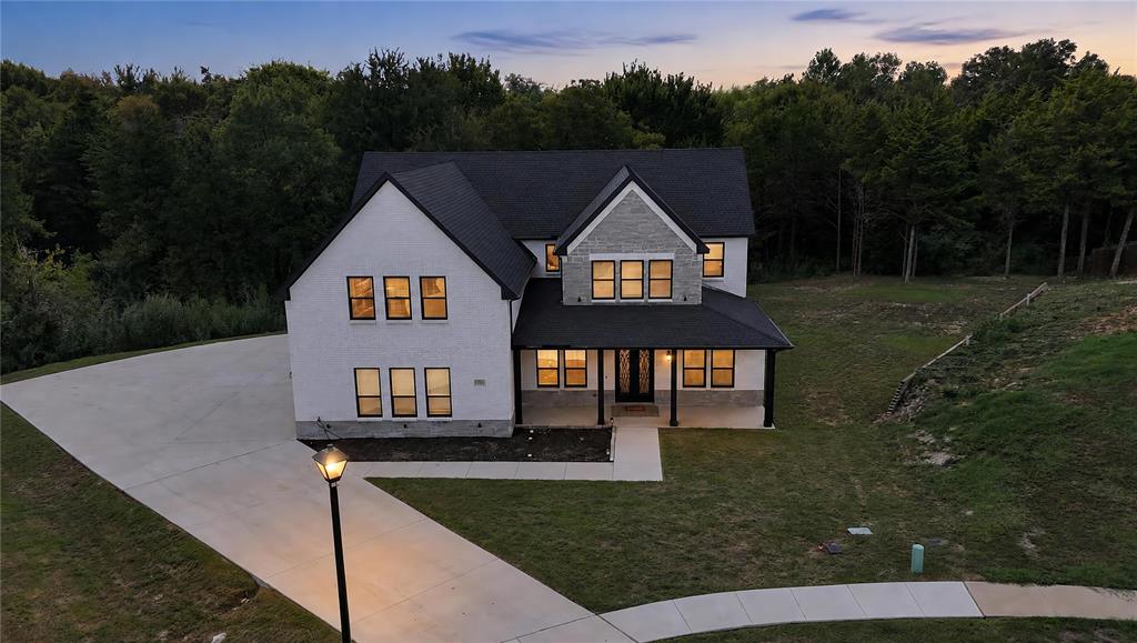 Two-story residence featuring a painted brick and stone exterior, steep-pitched shingle roof, covered front porch, and expansive concrete driveway