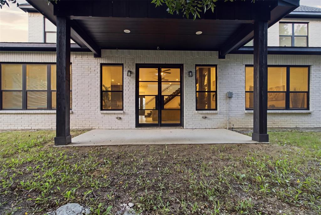 Covered rear patio featuring a white brick exterior, black-trimmed windows, and double glass-paned doors